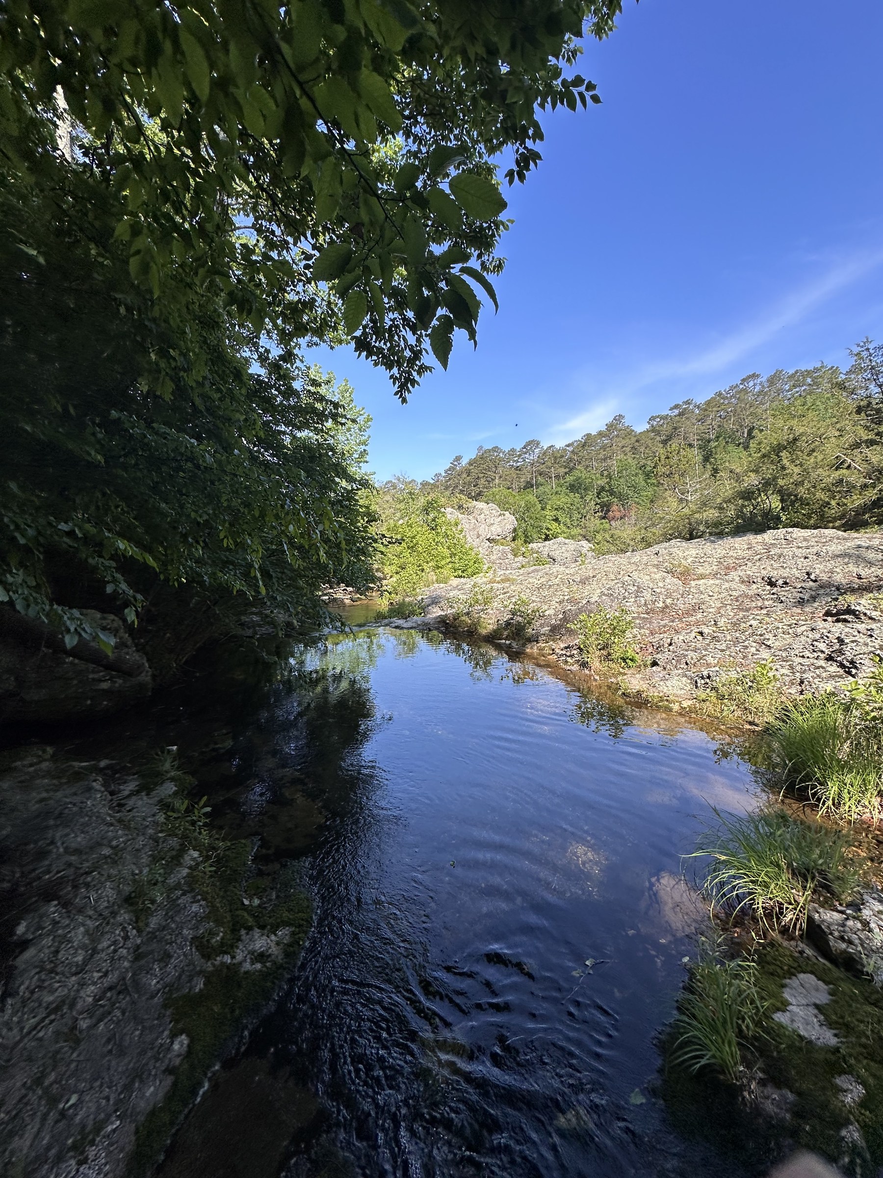 Still creek reflecting a distant rock face and blue sky