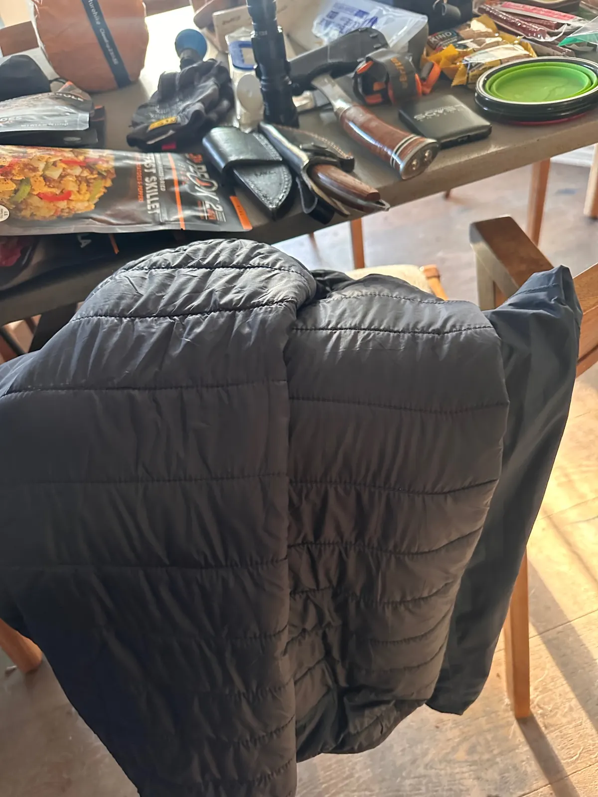 Puffy insulated jacket draped over a chair beside the gear pile