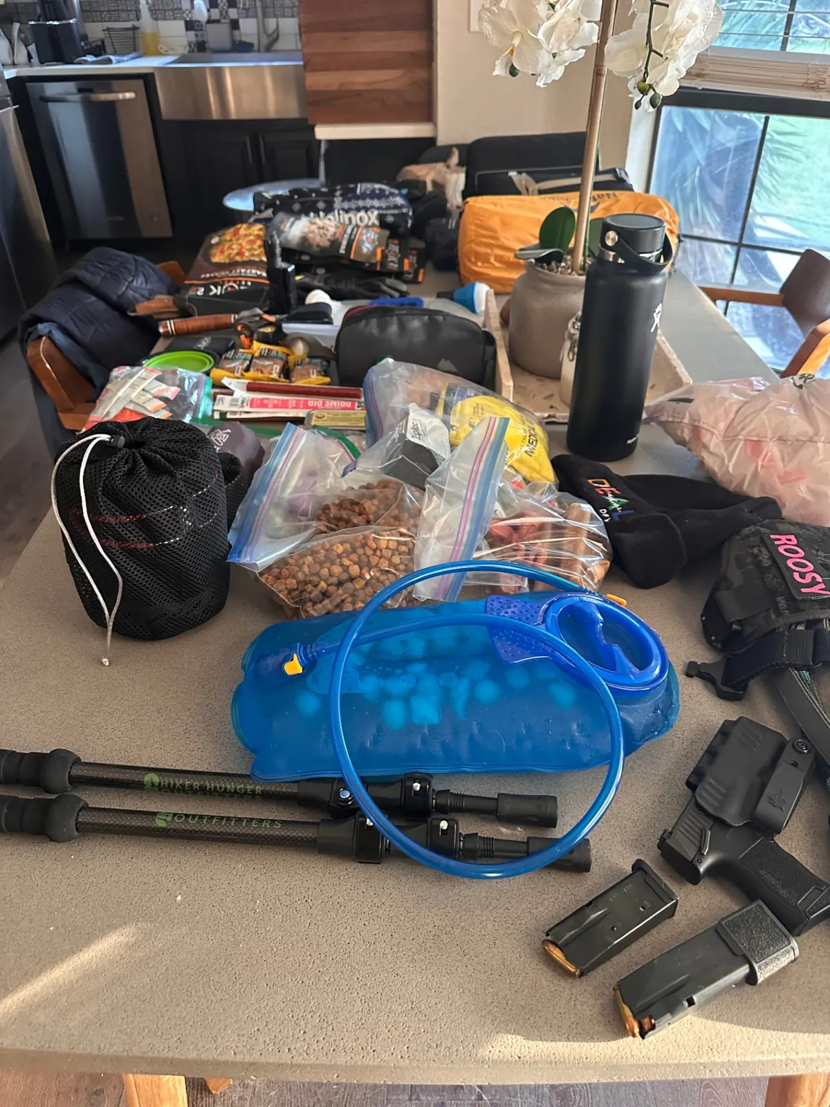 Food rations, hydration bladder, trekking poles, and sidearm on the counter