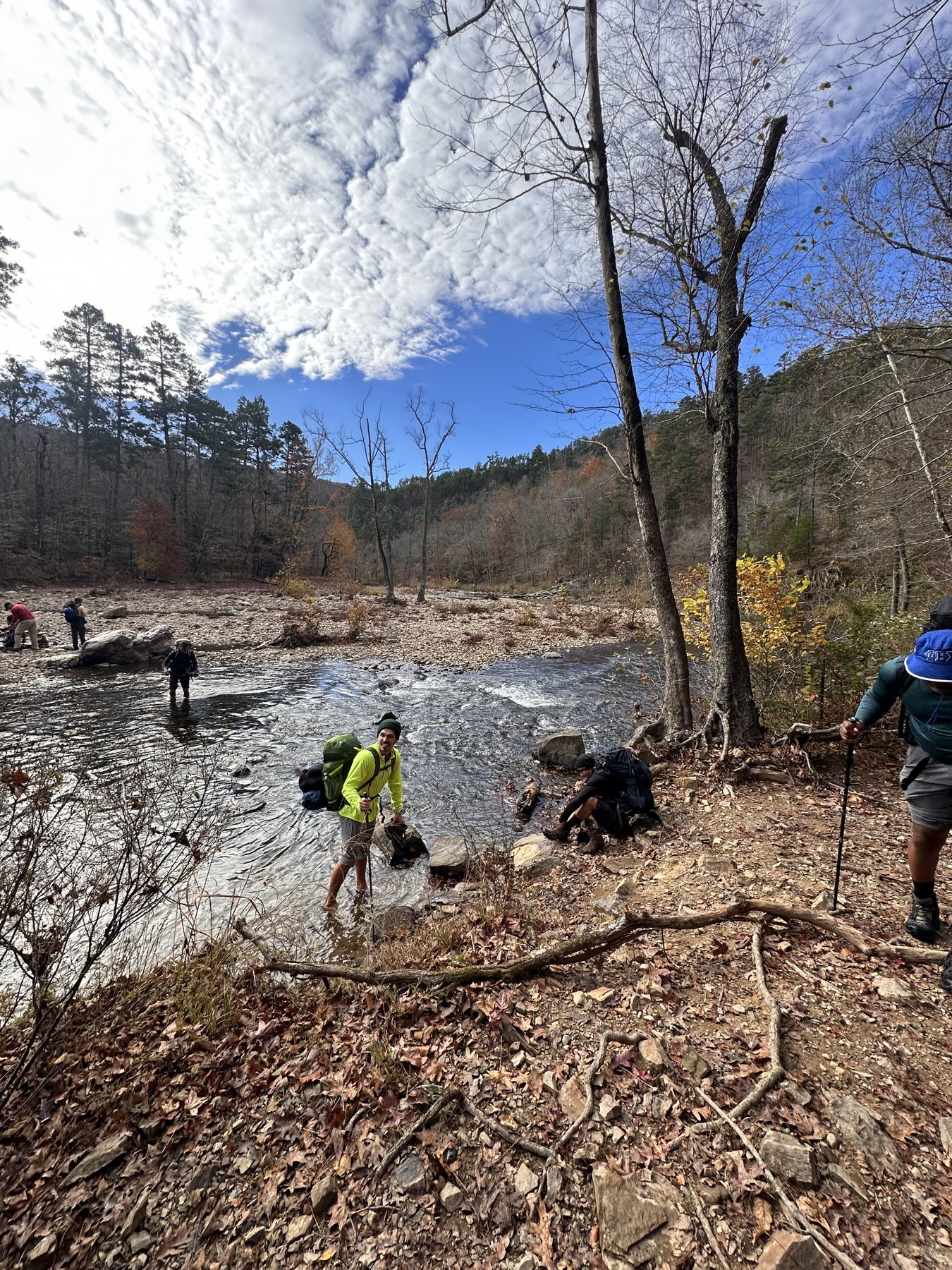 Group of hikers wading across a wide shallow river