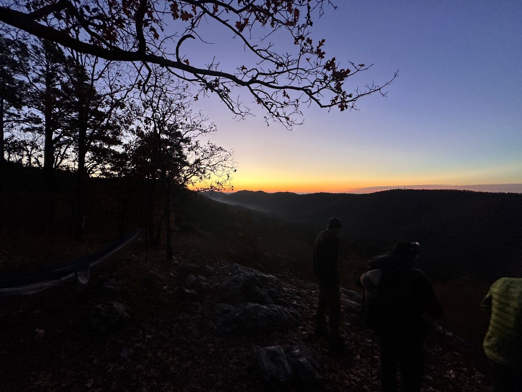 Silhouette of hikers against an orange sunset over rolling mountains