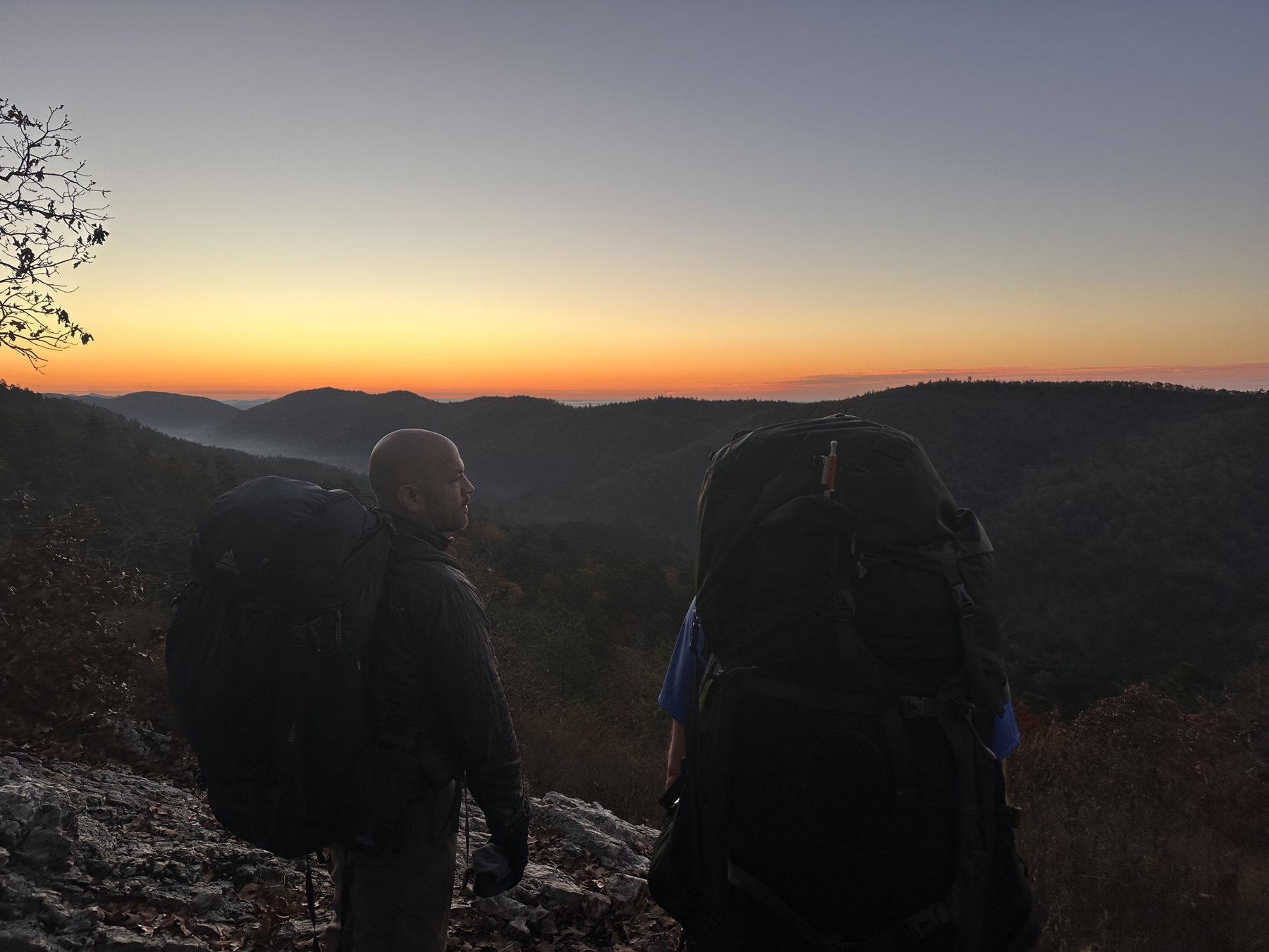Two backpackers seen from behind watching a mountain sunset
